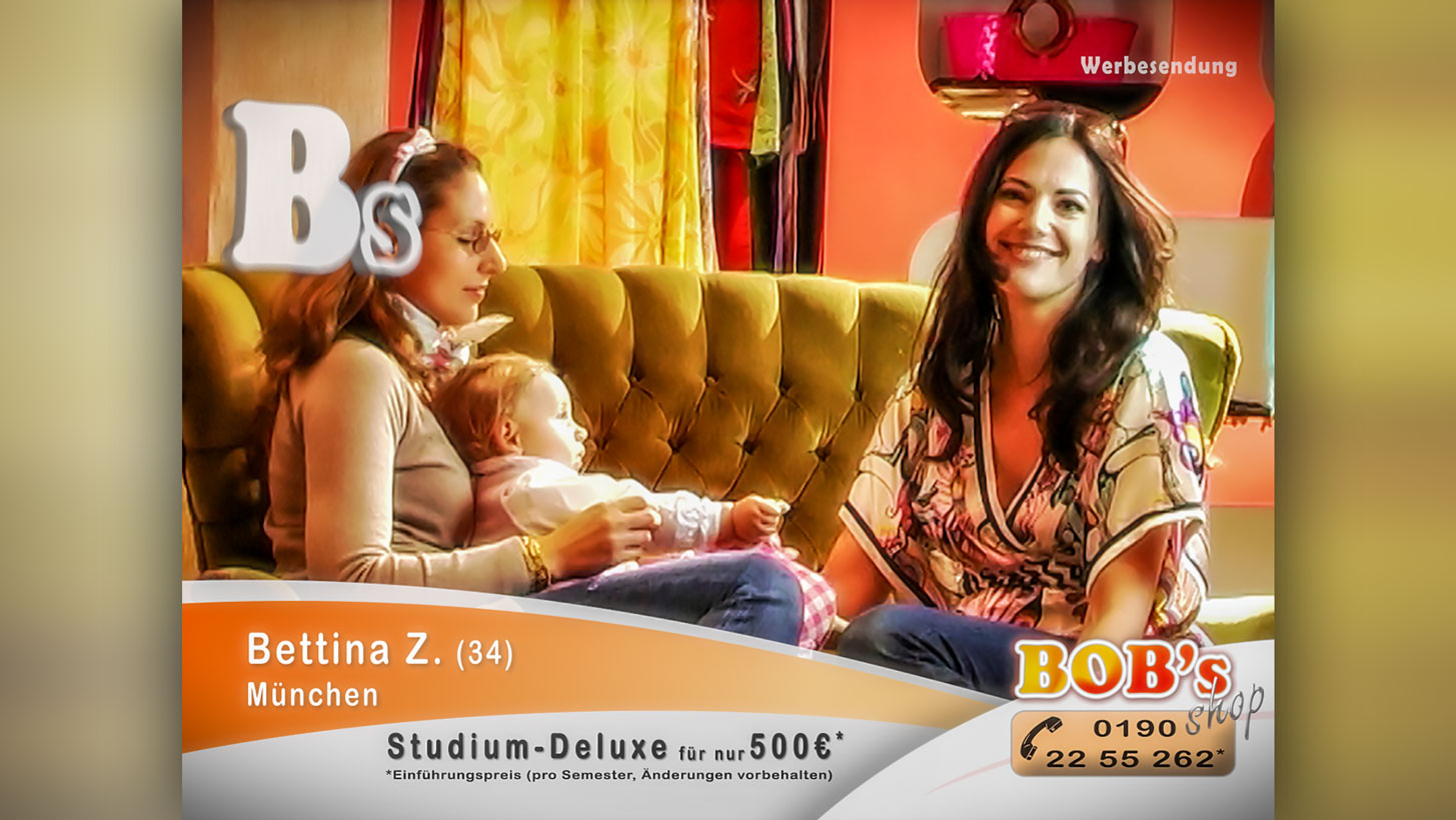 Szene aus dem Kurzfilm Studium-Deluxe: Die Schauspielerin Bettina Zimmermann sitzt auf einer gepolsterten Couch und lächelt in die Kamera. Neben ihr sitzt eine Frau mit einem kleinen Baby auf dem Schoß.